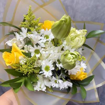 Bouquet of yellow roses and white daisies with green blooms wrapped in translucent paper
