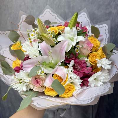 Handheld bouquet of pink lilies, yellow roses, and white daisies