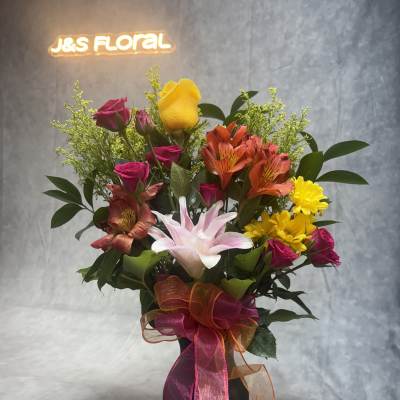 Mixed bouquet of roses, lilies, and daisies in a black vase with ribbon