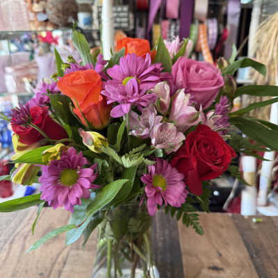 Mixed bouquet of pink, purple, and red flowers in a glass vase