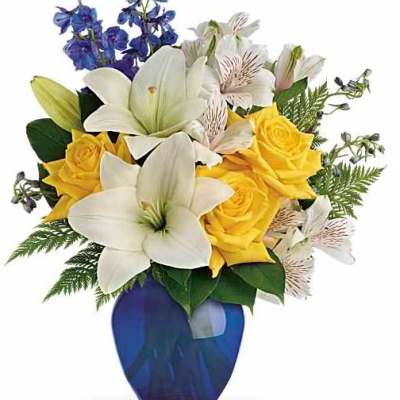Bouquet of white lilies, yellow roses, and blue flowers in a blue vase