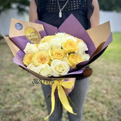 Bouquet of yellow and white roses wrapped in purple and tan paper