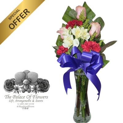 Mixed bouquet of pink, white, and red flowers in a tall glass vase with a purple bow