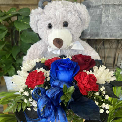Teddy bear holding a bouquet of red, blue, and white flowers