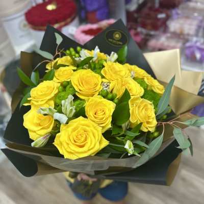 Hand-tied bouquet of bright yellow roses with white blooms and green accents wrapped in dark and gold paper