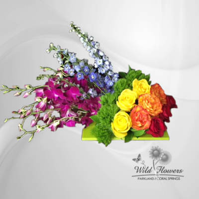 Colorful floral arrangement with orchids, roses, and blue spikes on a green base