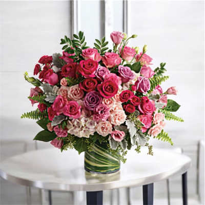 Large arrangement of pink and lavender roses in a glass vase lined with green leaves