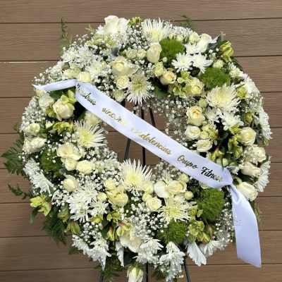 White floral wreath on an easel with a ribbon across the center