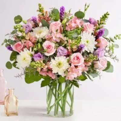 Large pastel arrangement of pink roses, white mums, and lavender blooms in a clear glass vase