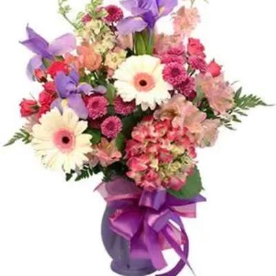 Mixed bouquet of pink, purple, and white flowers in a vase with a purple ribbon