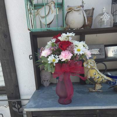 Bouquet of red roses, white daisies, and pink carnations in a frosted vase with a red ribbon