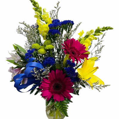 Bright mixed bouquet with pink gerbera daisies, yellow snapdragons, and blue flowers in a glass vase