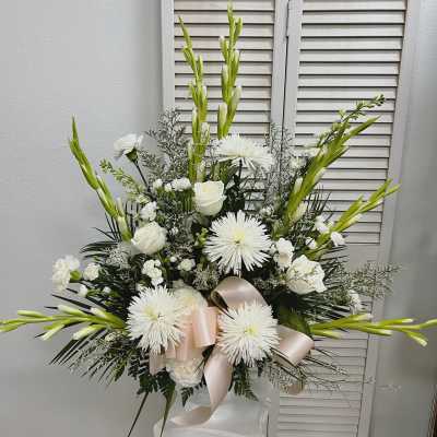 Tall white floral arrangement with lilies, roses, and ribbon in a vase