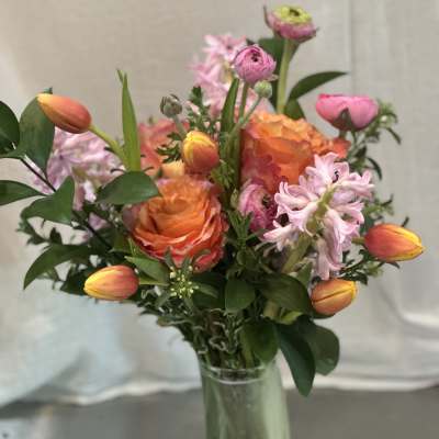 Mixed bouquet with orange roses, pink tulips, and pale pink blooms in a glass vase