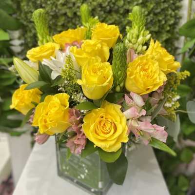 Yellow rose and pink alstroemeria arrangement with white lilies in a square glass vase