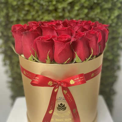 Round box of tightly packed red roses in a gold hatbox with a red ribbon bow