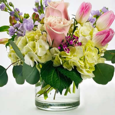 Pink roses and tulips arranged with pale hydrangeas in a clear glass vase