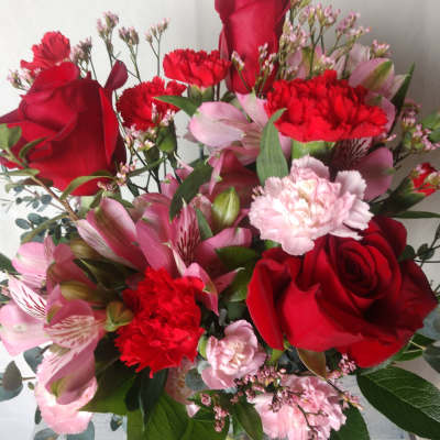 Bouquet of red roses, pink alstroemeria, and carnations in a glass vase