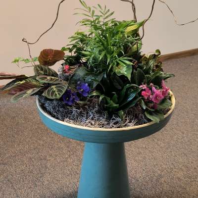 Mixed potted plants and small purple and pink flowers in a pedestal planter
