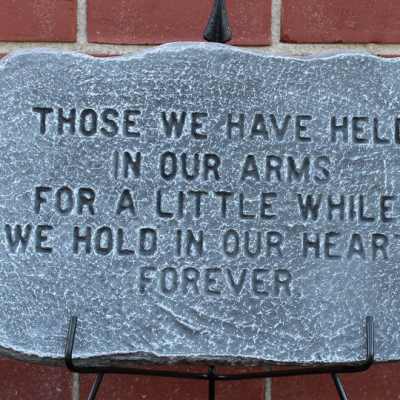 Engraved memorial stone plaque on a stand against a brick wall.