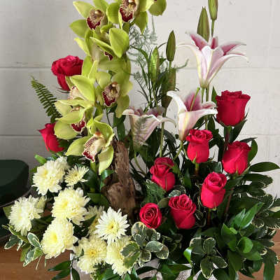 Mixed floral arrangement with red roses, green orchids, white lilies, and white mums in a silver box.
