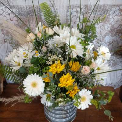 Mixed white and yellow flowers arranged in a metal bucket