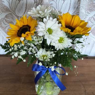 Sunflowers and white daisies in a glass jar with a blue ribbon