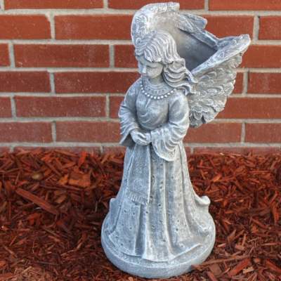 Silver angel statue planter standing against a brick wall