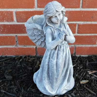 Small angel statue in a long dress standing against a brick wall