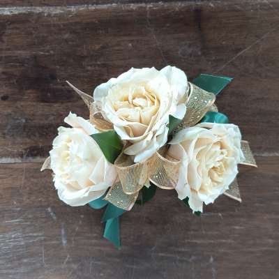 Three cream roses with a gold ribbon on a wooden surface