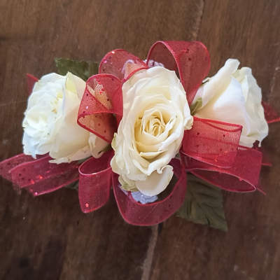 White rose corsage with red ribbon on a wooden surface