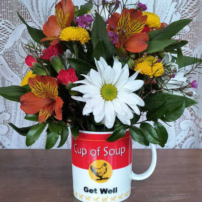 Mixed flowers arranged in a soup mug with a Get Well message