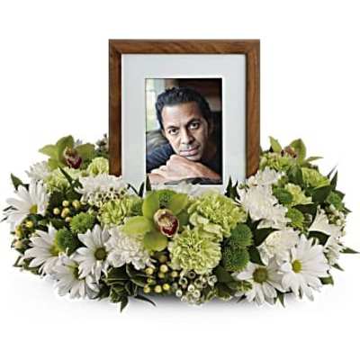 Framed photo surrounded by white and green funeral flowers