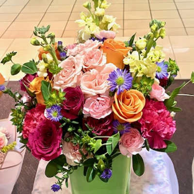 Mixed bouquet of roses, carnations, and purple daisies in a green vase