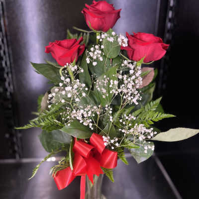 Three red roses in a glass vase with baby's breath and a red ribbon