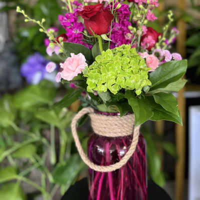 Bouquet of red roses, pink flowers, and green hydrangea in a glass vase
