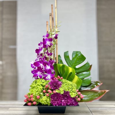 Tall modern arrangement with purple orchids, green hydrangeas, and mums in a black rectangular container