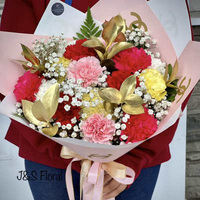 Handheld bouquet of pink, red, yellow, and white carnations with baby's breath