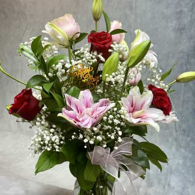 Mixed bouquet of red roses, pink lilies, and white baby's breath in a glass vase