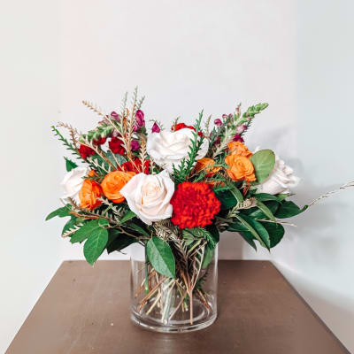 Bouquet of orange, white, and red roses in a clear glass vase