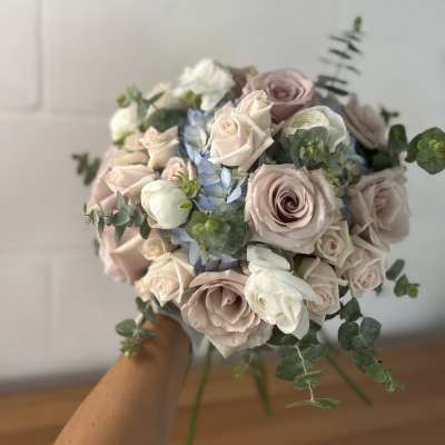 Handheld bouquet of blush roses, white blooms, and blue flowers