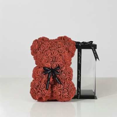 Red rose teddy bear beside a black gift box with ribbon