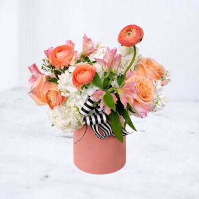 Peach and pink flower arrangement in a pink cylindrical box with a striped ribbon