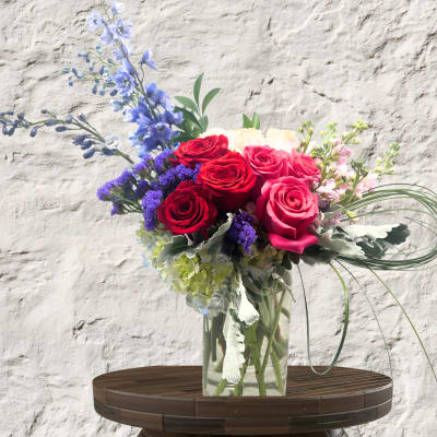 Bouquet of red and pink roses with blue flowers in a glass vase