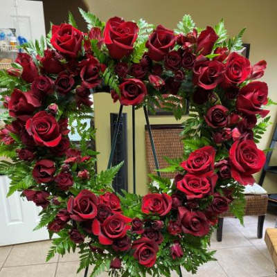 Heart-shaped wreath of red roses with abundant ferns on a standing easel