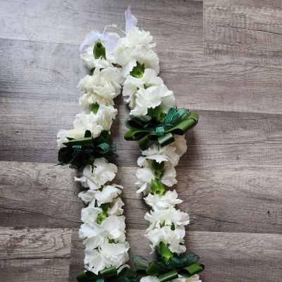 White carnation lei with green ribbon bows on a wood surface