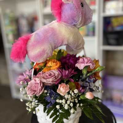 Unicorn plush topper above a colorful flower basket in a white container