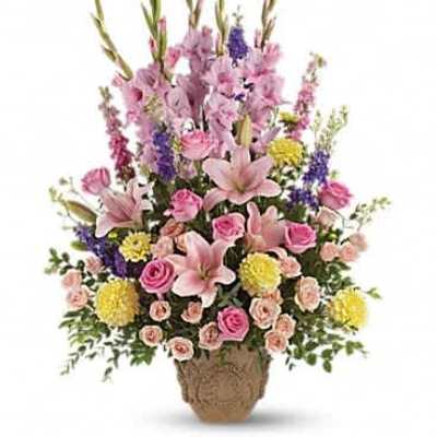 Tall pastel arrangement with pink lilies, roses, yellow mums and purple flowers in a tan urn.