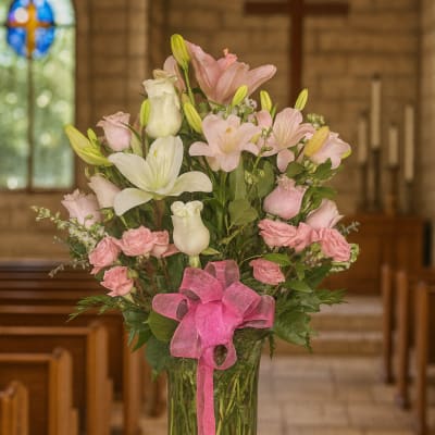 Pink and white flowers arranged in a glass vase with a pink ribbon