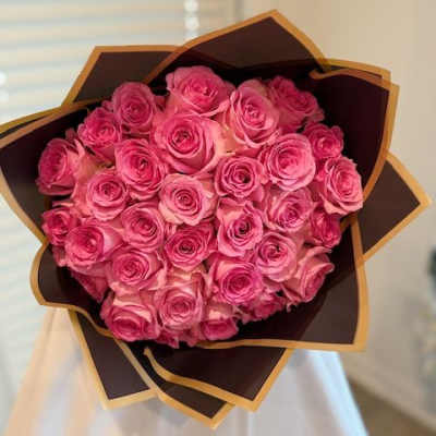 Bouquet of pink roses wrapped in dark paper with gold trim